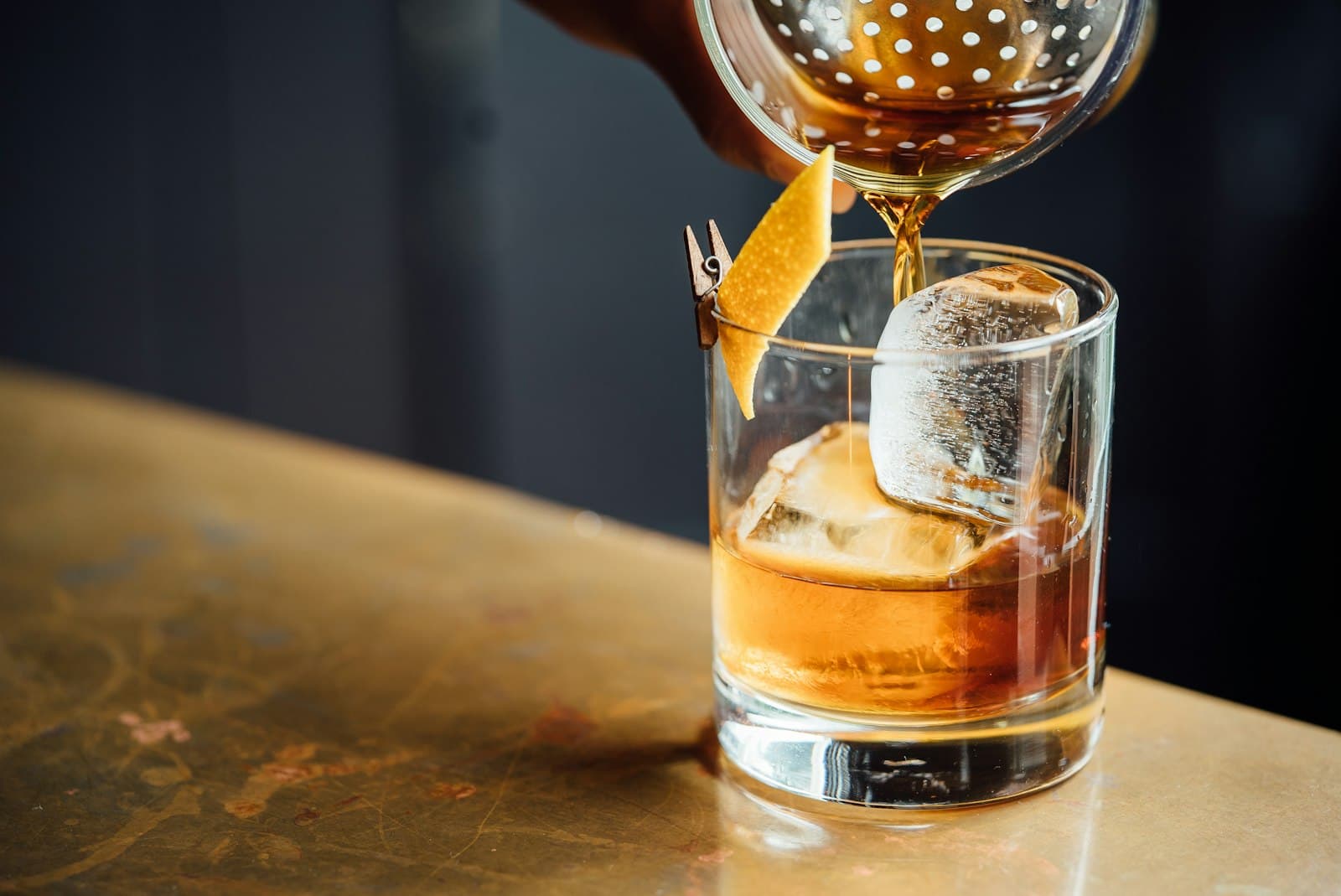 Cocktail ambré versé au tamis sur un grand glaçon taillé