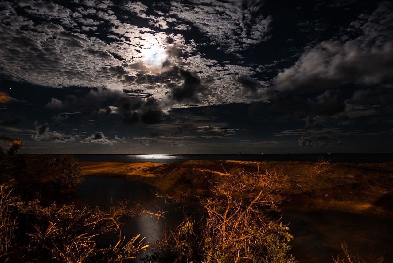 Pleine lune perçant les nuages au-dessus d'une mer argentée