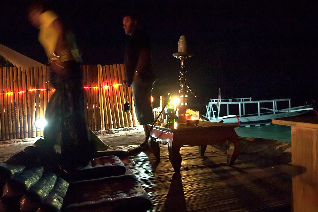 Chicha fumant à la nuit tombée sur une terrasse en bois face à la mer